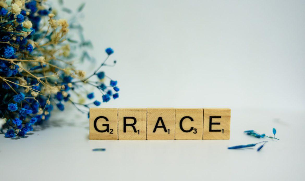 a wooden block that says grace next to a bouquet of flowers